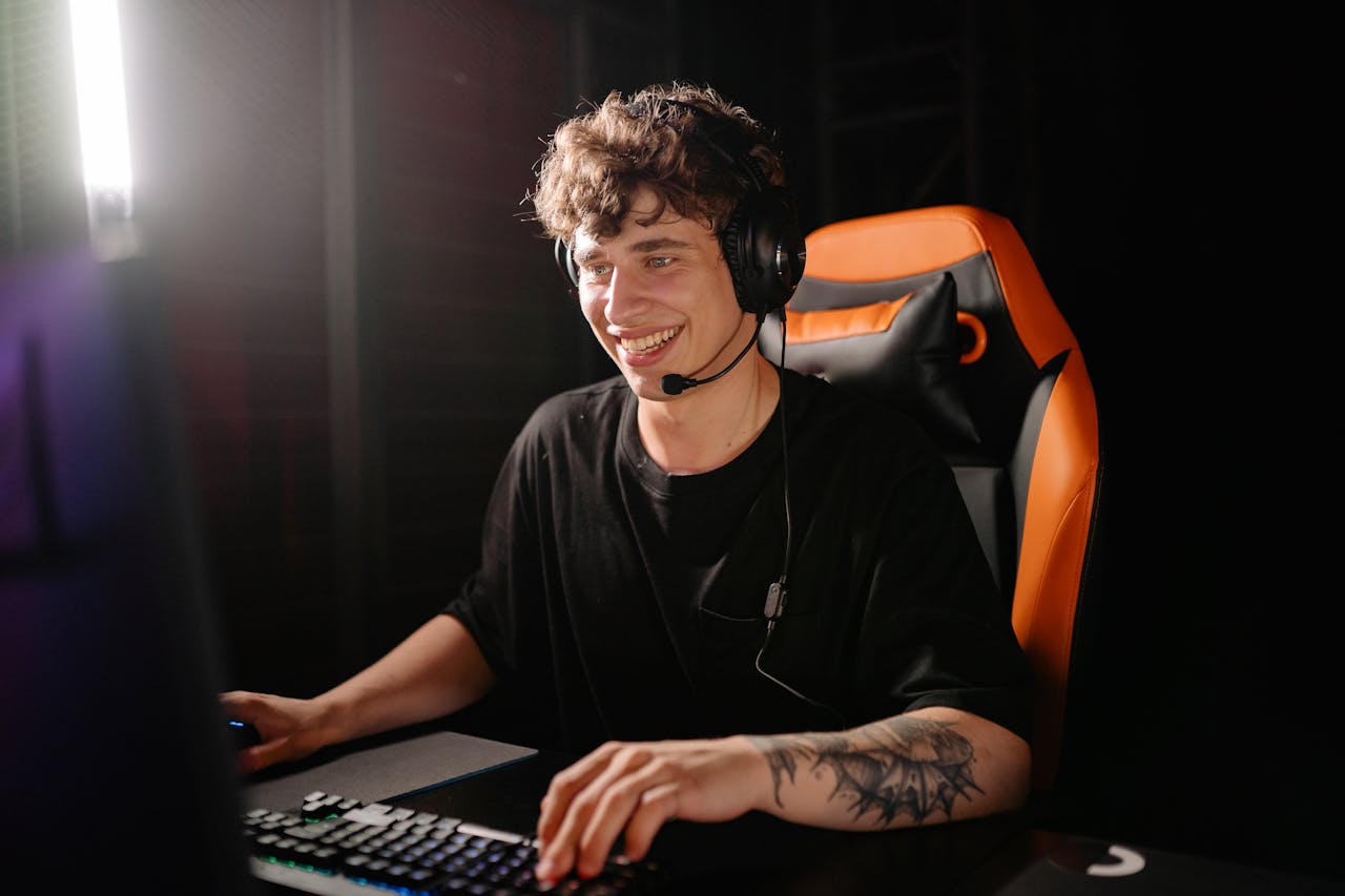Photo of a Man in a Black Shirt Smiling while Playing on a Computer